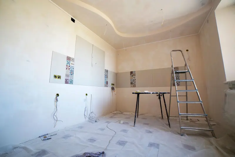 Pièce en cours de rénovation : murs enduits, carreaux de ciment posés par endroits, escabeau et bâche de protection au sol